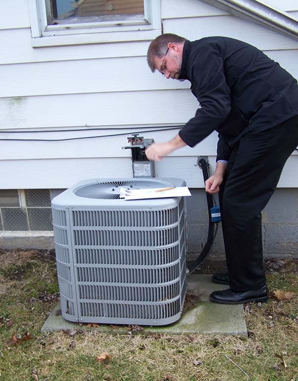 HVAC technician working at a residential outdoor condensing unit beside a home.