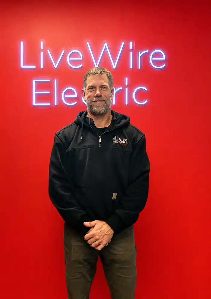 Brian McKee, founder and owner of Live Wire Electric, standing in front of the company's red Live Wire Electric sign.