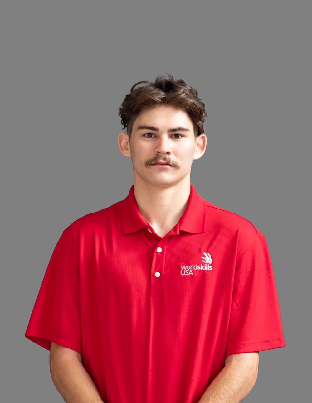 Official SkillsUSA portrait of Charles Goede wearing a red WorldSkills USA polo shirt against a gray background.