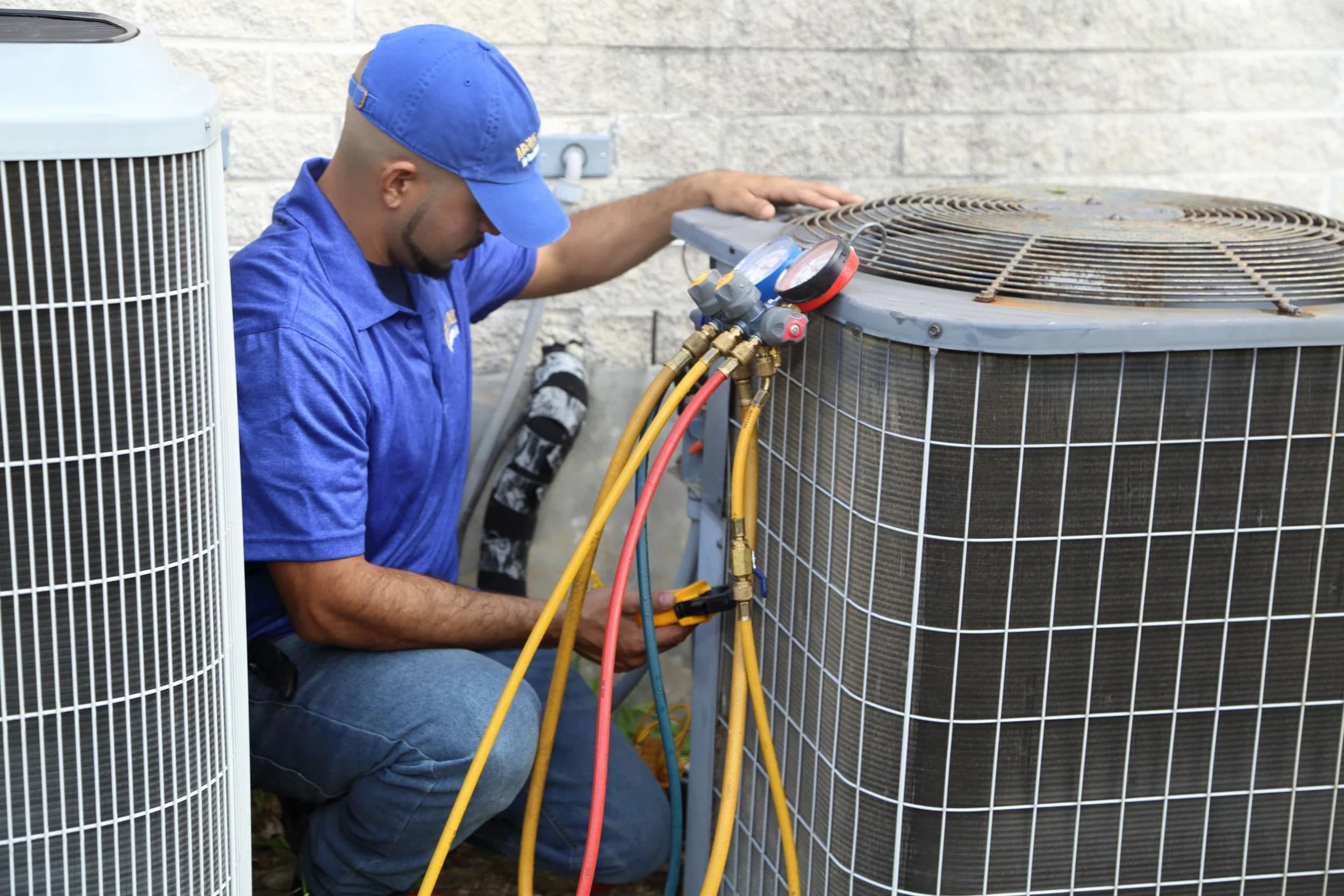 HVAC technician using manifold gauges while servicing an outdoor air-conditioning condenser.