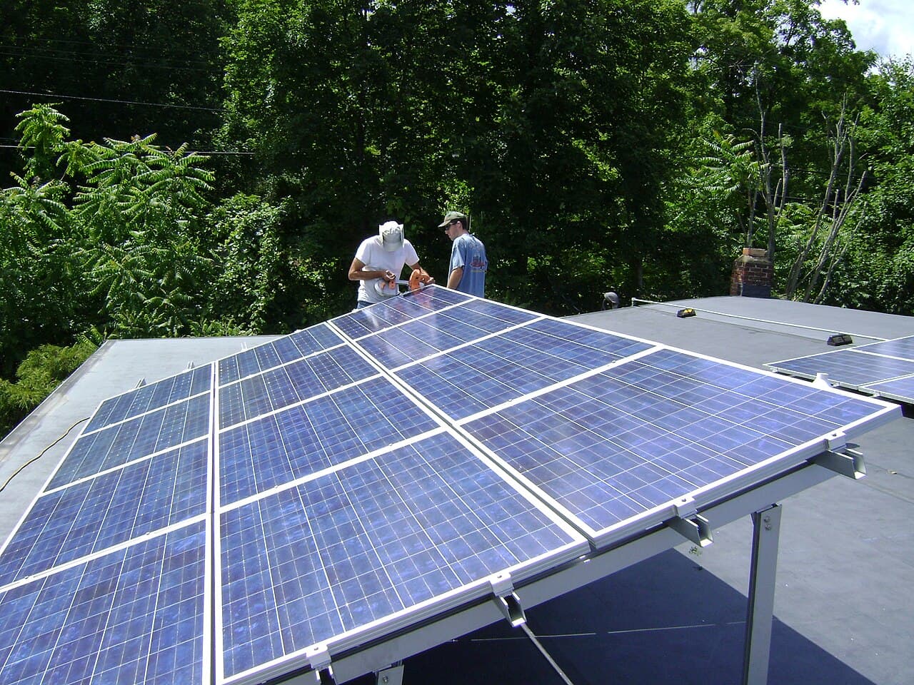 Two workers install a tilted photovoltaic panel array on a rooftop near Poughkeepsie, New York.