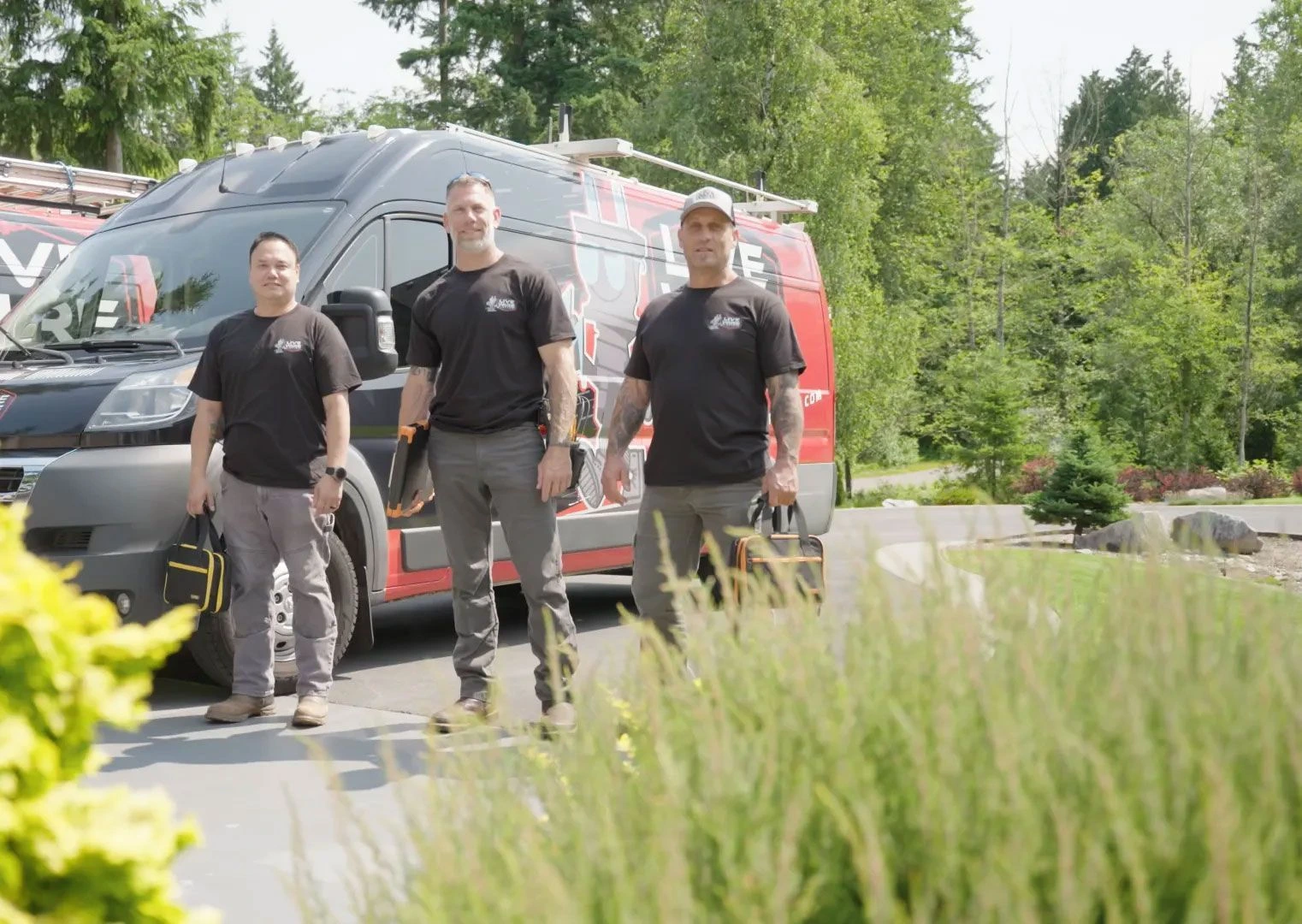 Three Live Wire Electric team members carrying tools beside a branded service van outside a home.