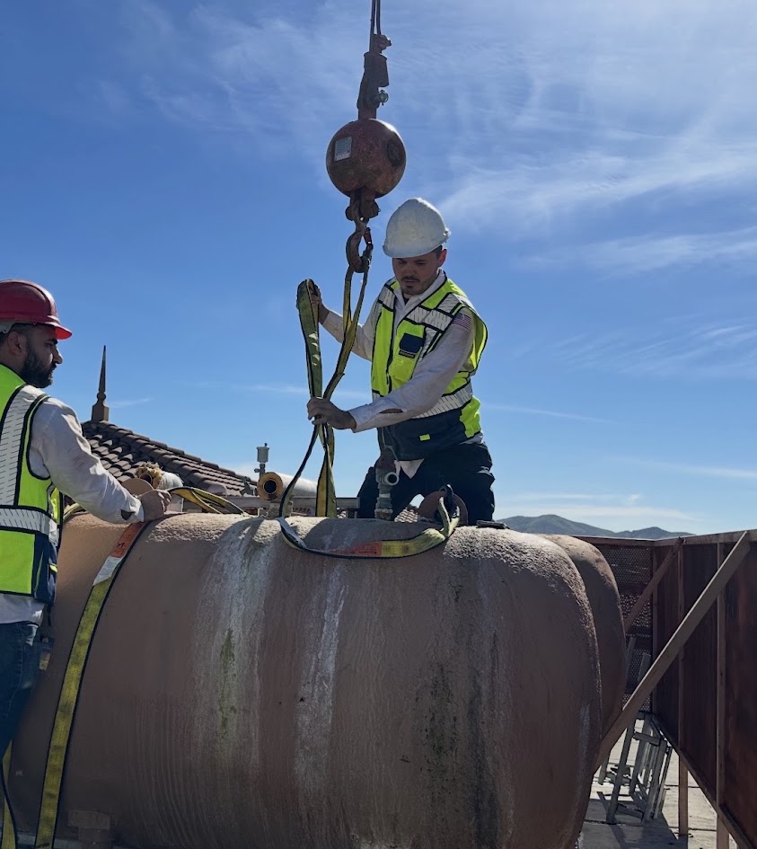 TradeVulcan founder Brandon Stowe wearing a hard hat and high-visibility safety vest while working with rigging equipment on a jobsite.
