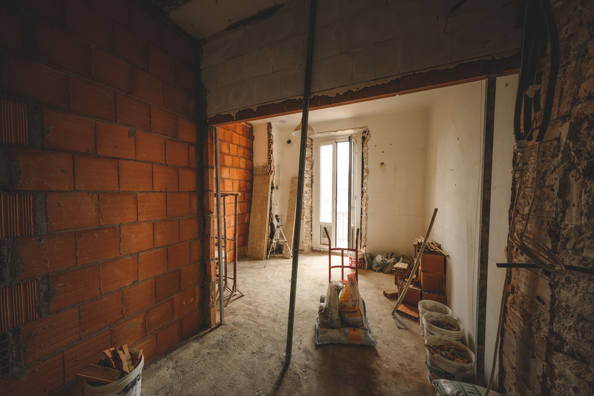 A room under renovation with exposed brickwork, temporary supports, tools and bagged building materials.