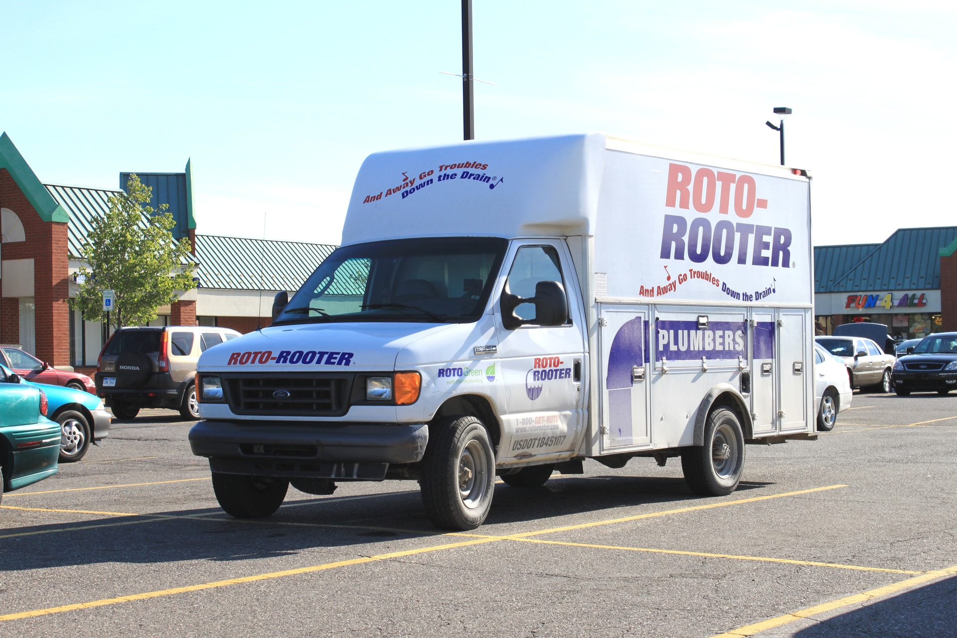A white Roto-Rooter service vehicle with red and blue branding parked in a Michigan shopping-center lot.