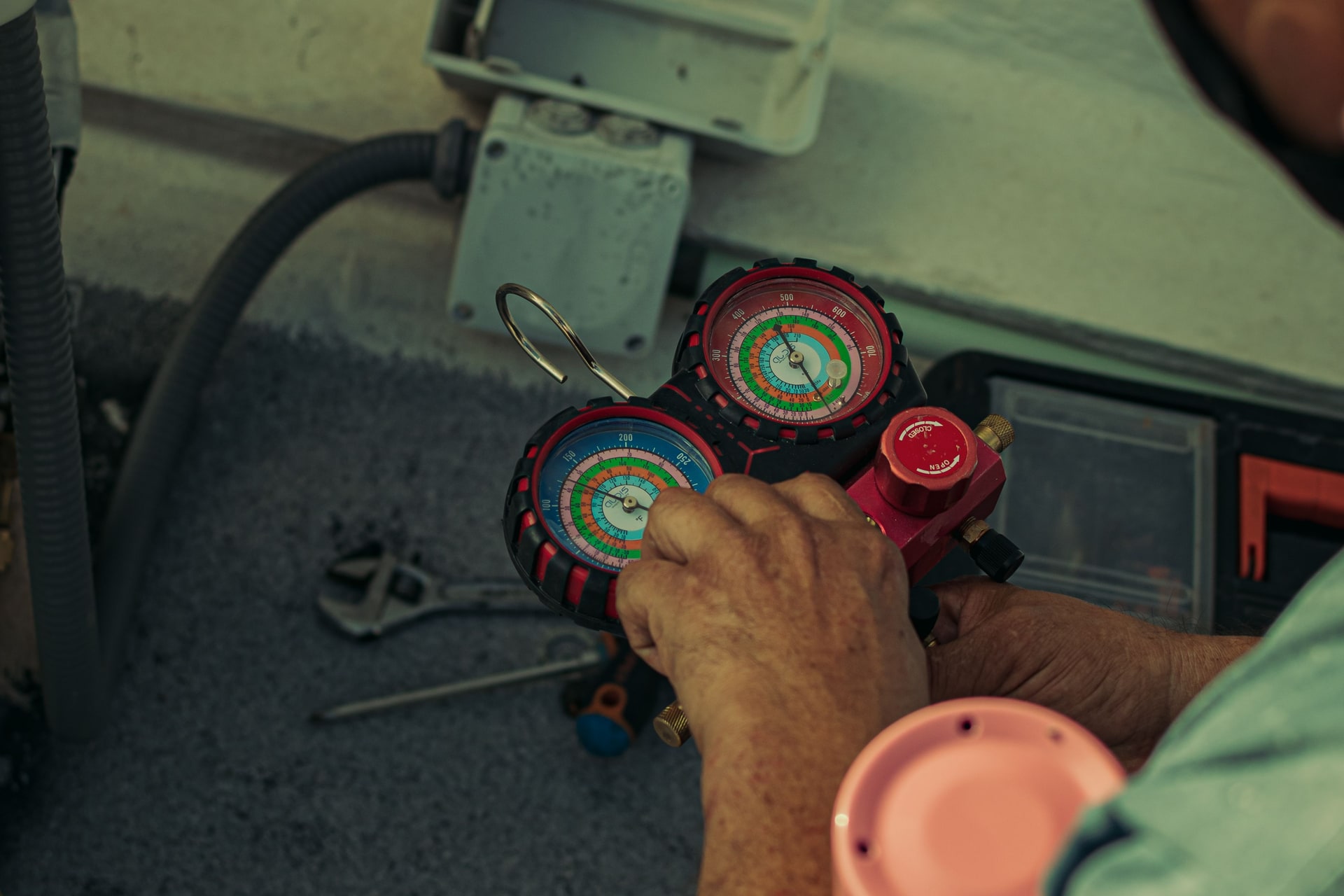 A technician holds blue and red refrigerant manifold gauges beside air-conditioning equipment.