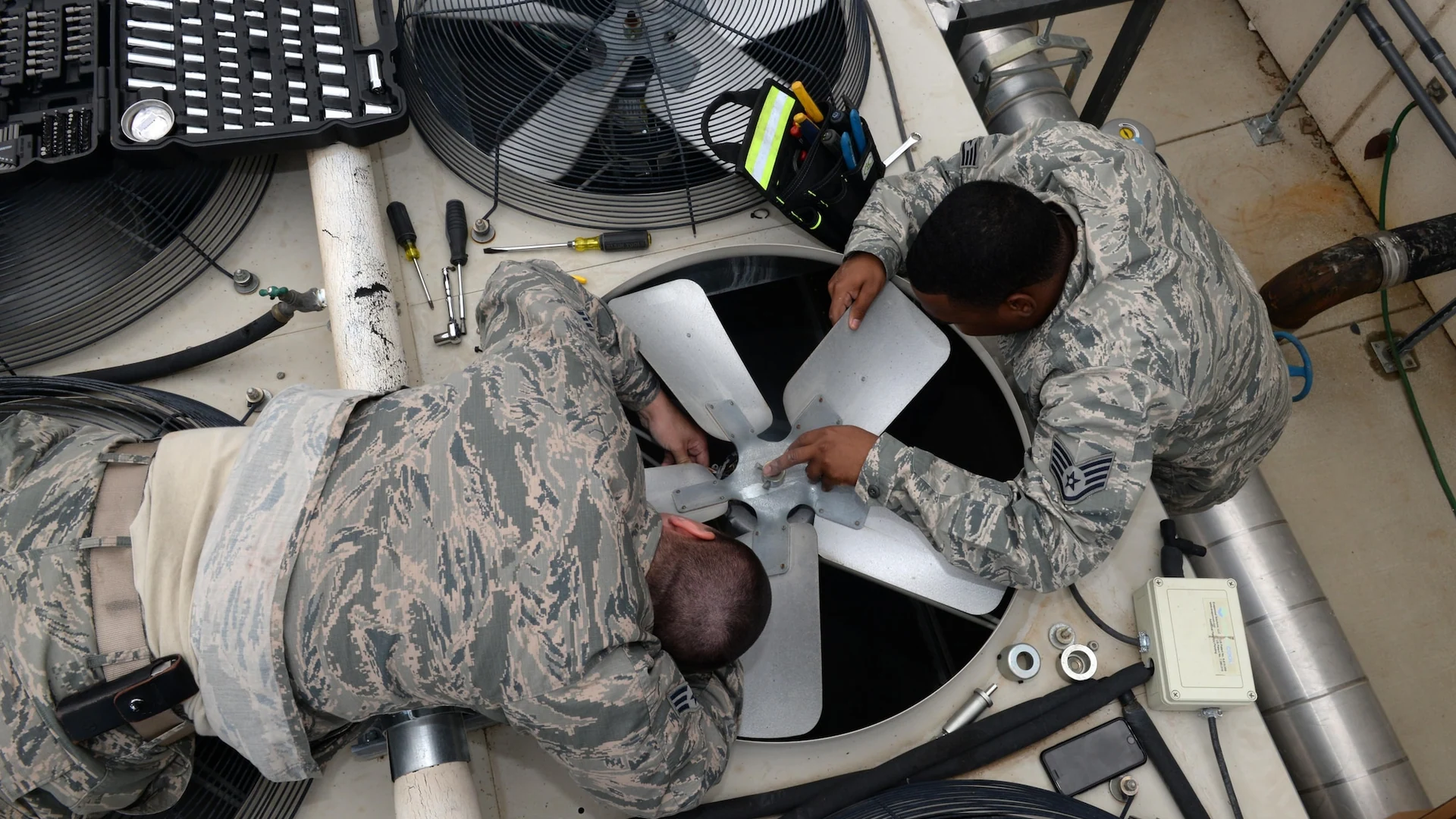 Two U.S. Air Force HVAC technicians work on a large cooling-unit fan at Beale Air Force Base in California.