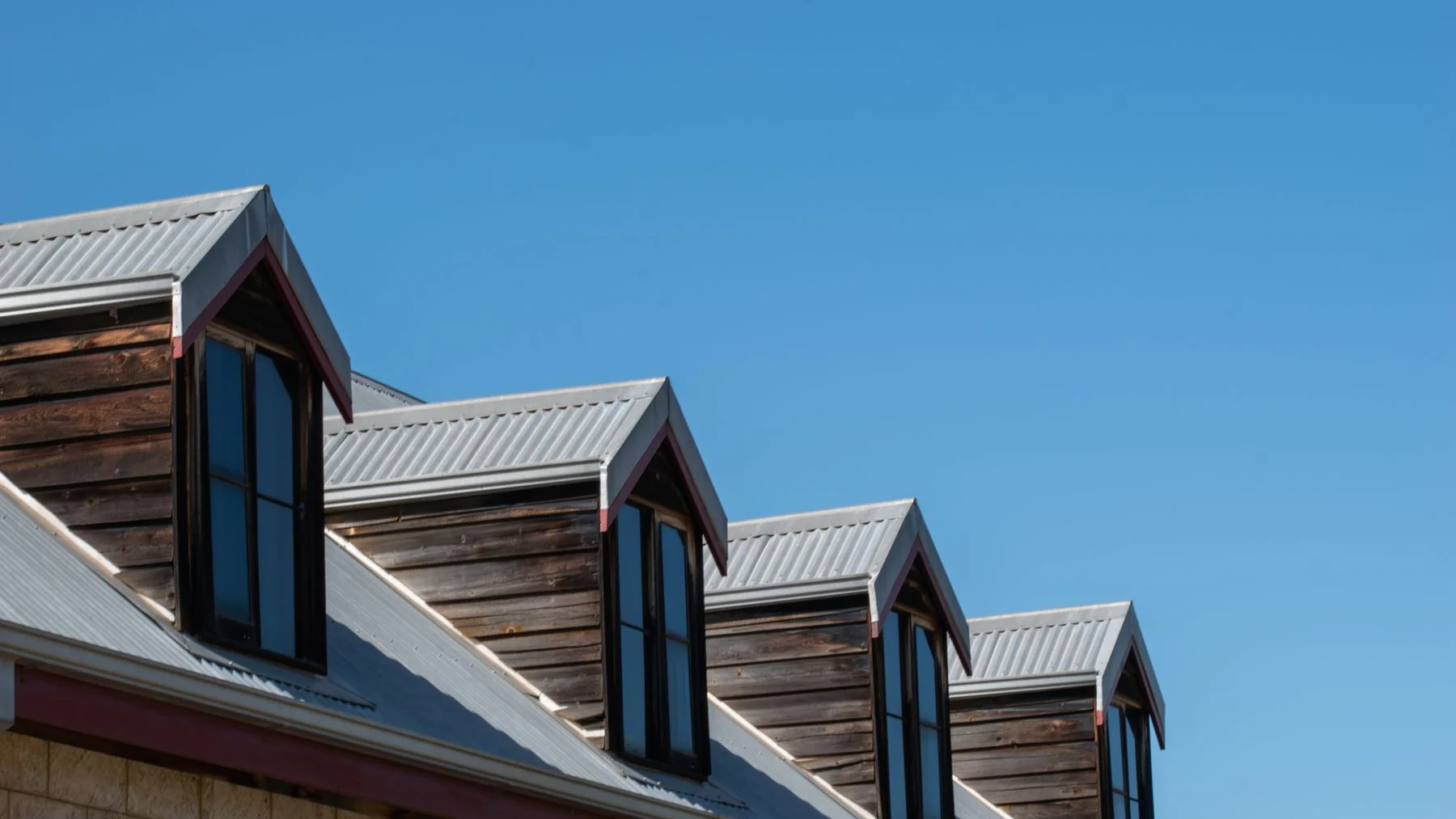 Metal roofing and a row of timber-clad dormer windows beneath a clear blue sky.