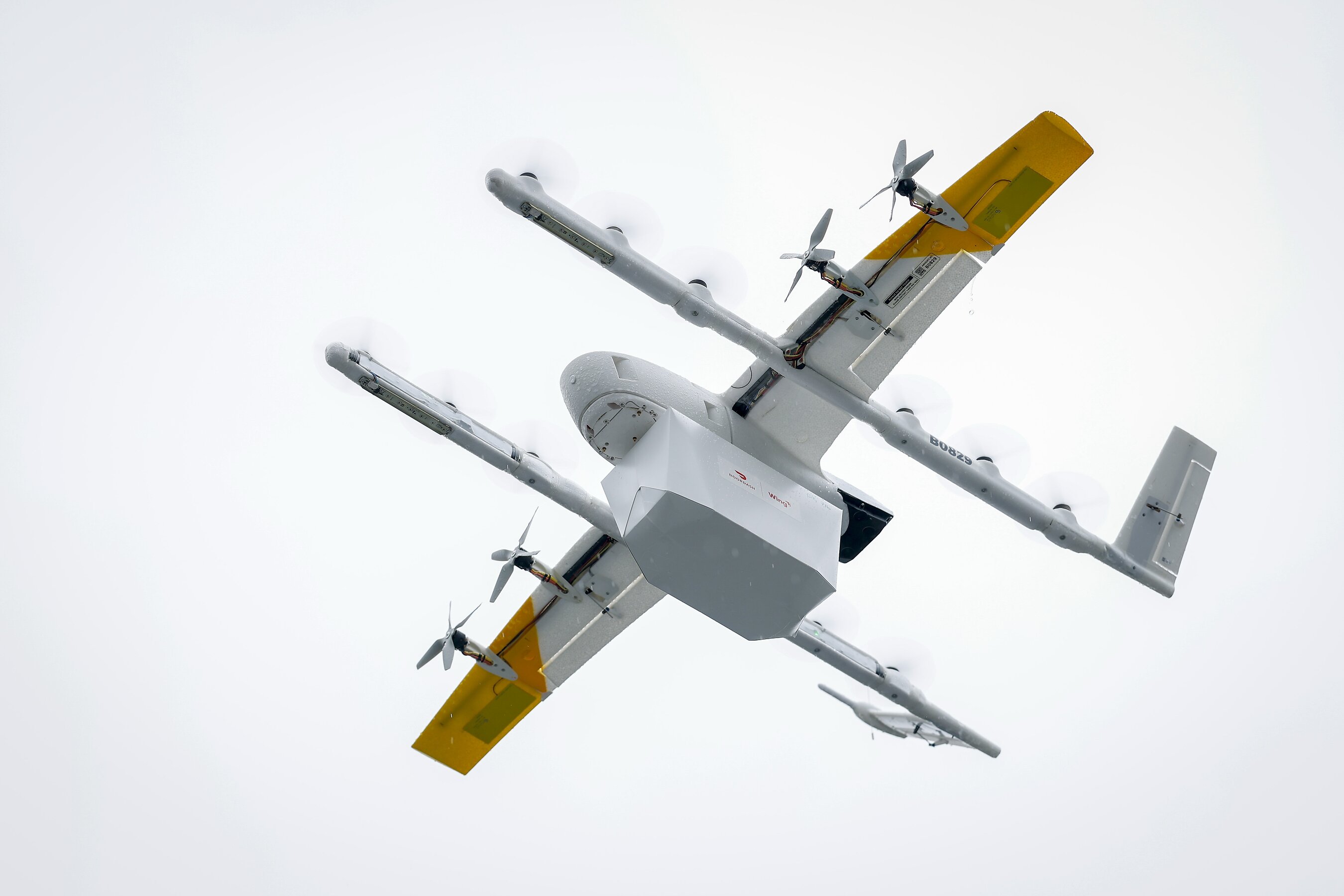 Real Lowe’s press photograph looking up at a Wing delivery drone carrying a white package in flight.