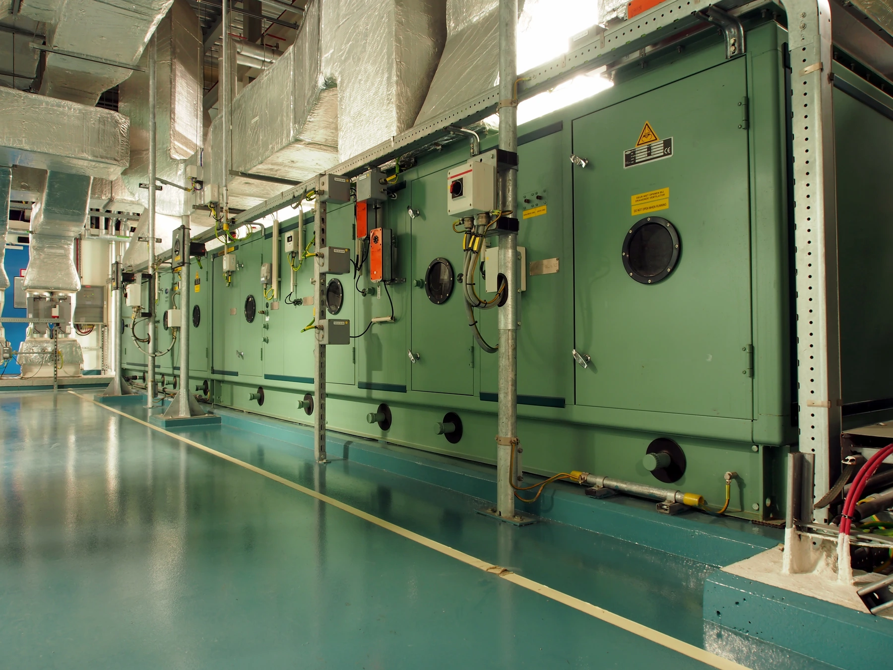 Large green HVAC air-handling equipment beneath insulated metal ductwork.