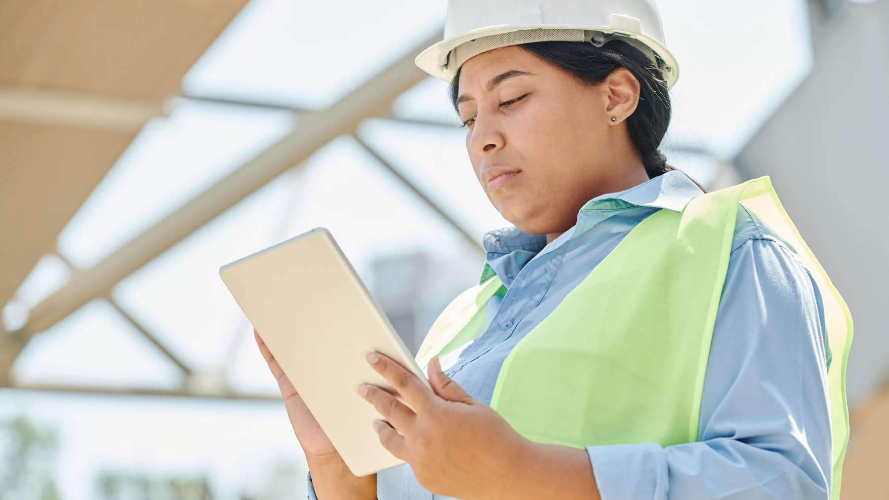 Construction professional in a hard hat using a digital tablet at an active jobsite.